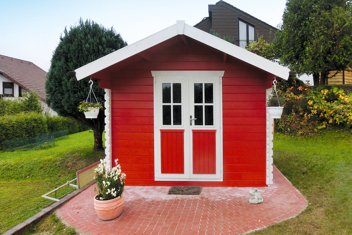 Rotes Gartenhaus Porto mit weißen Doppeltüren und zwei hängenden Blumentöpfen an den Ecken
