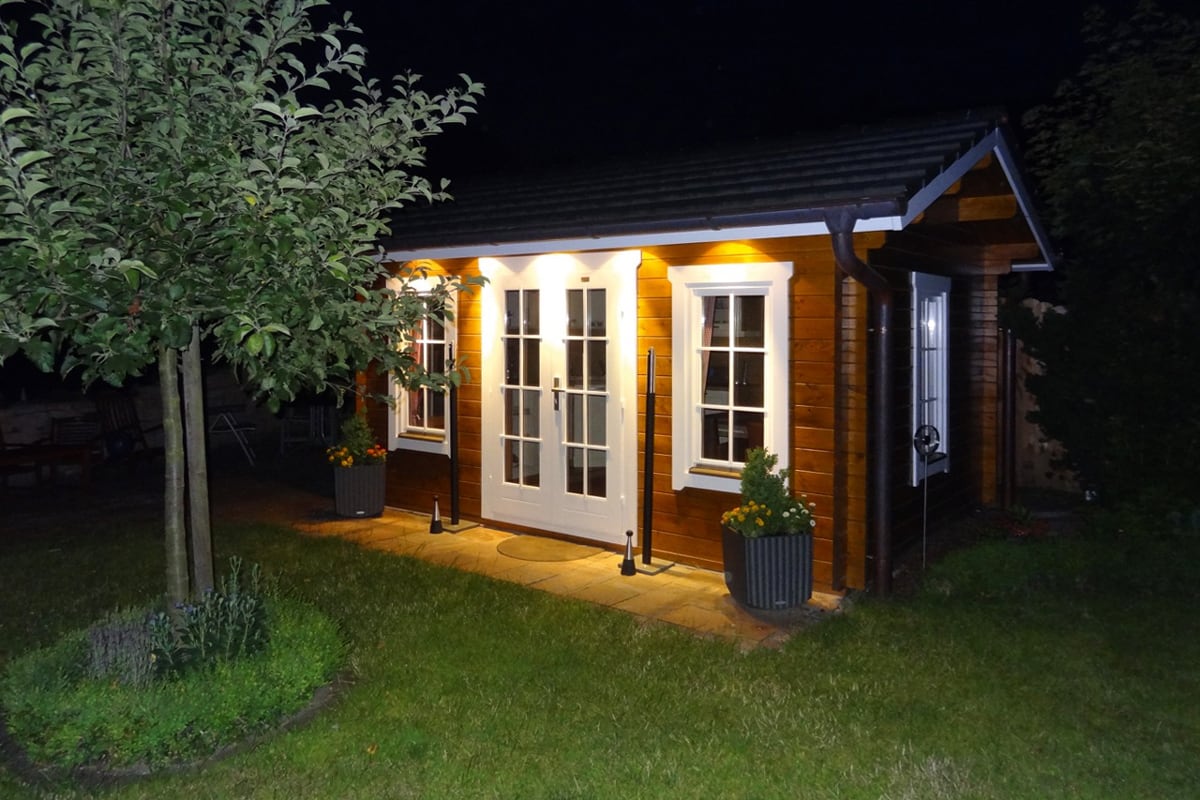 Beleuchtetes Gartenhaus bei Nacht mit weißen Fenstern