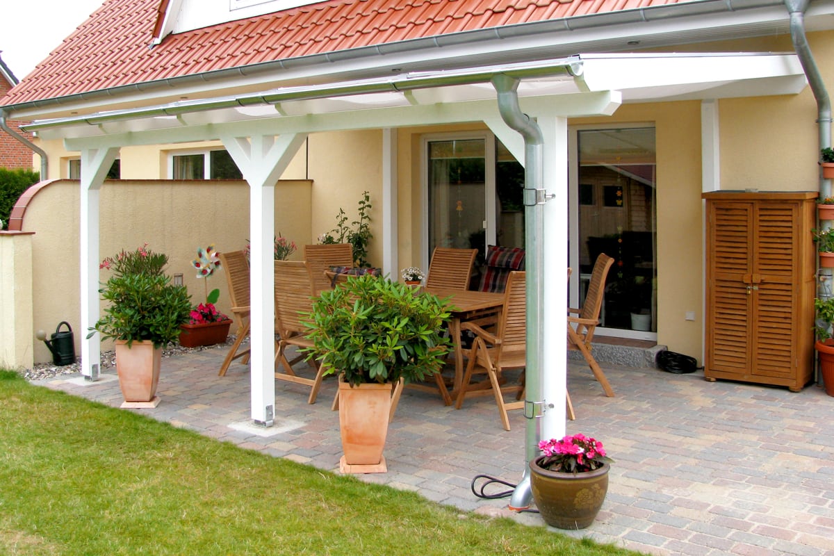 Die weiße Holzüberdachung wirkt modern und stabil zugleich. Sie bietet einen geschützten Essbereich direkt am Haus.