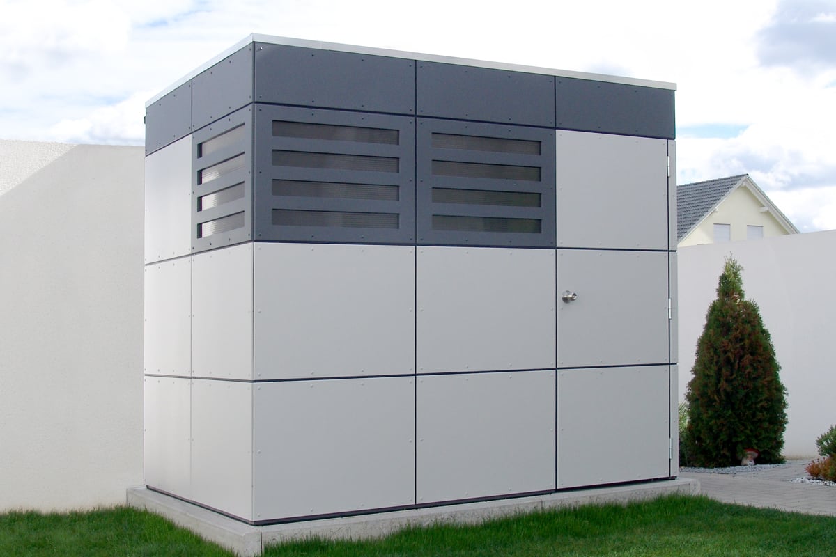 Modernes graues Gerätehaus CrossCube in Würfelform auf Rasen vor weißer Mauer und Haus
