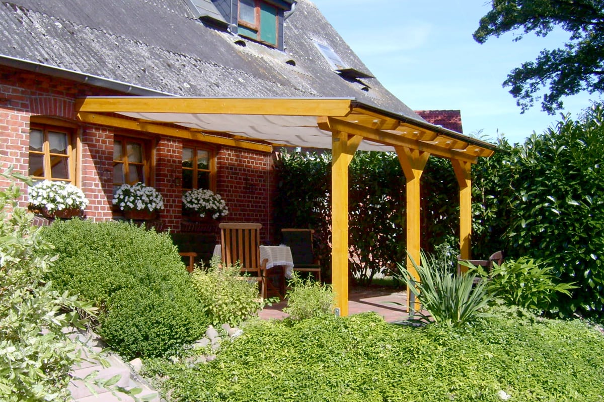 Eine robuste Terrassenüberdachung aus hellem Holz mit leicht geneigtem Dach.