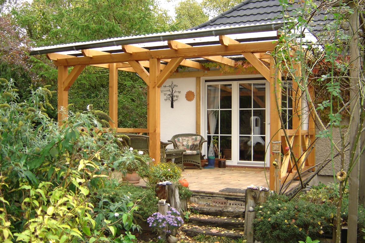 Eine gemütliche Holzüberdachung schützt die Terrasse mit Sitzmöbeln, die harmonisch in den grünen Garten eingebettet ist.