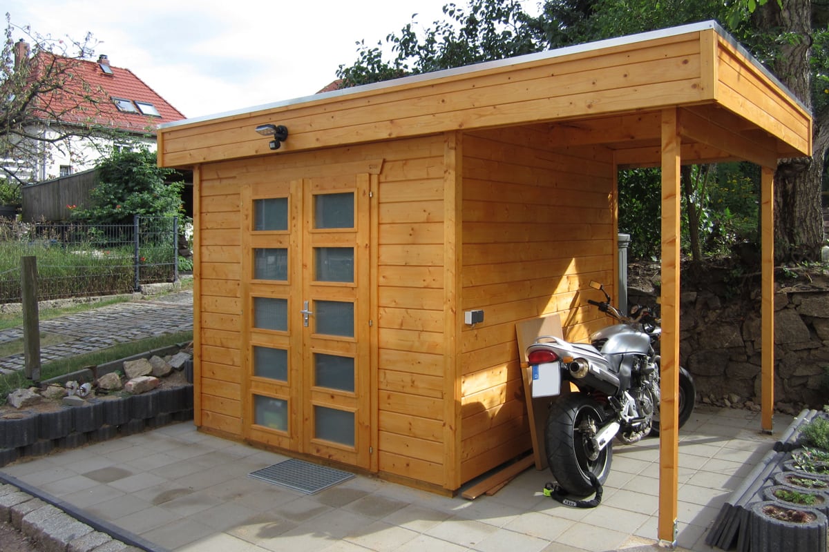 Holzhaus Venlo 2 mit Flachdach und Glastüren, daneben überdachter Stellplatz mit Motorrad