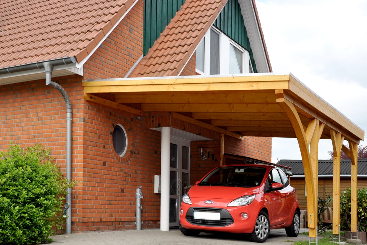 Carport aus Wandanbau mit einem Einfahrtsbogen aus Leimholz
