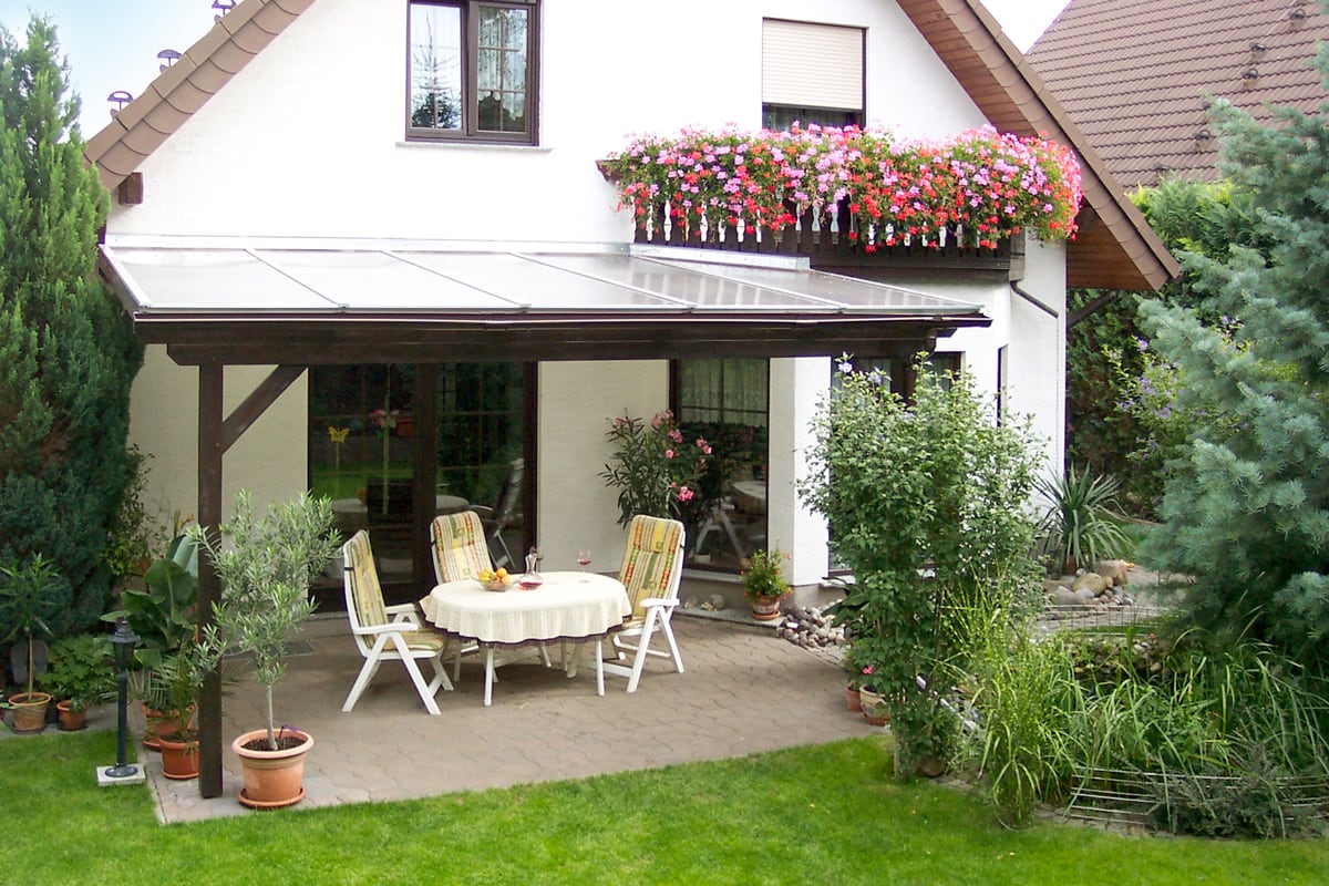 Eine überdachte Terrasse mit dunkler Holzkonstruktion und Sitzgruppe lädt zum Verweilen im blühenden Garten ein.