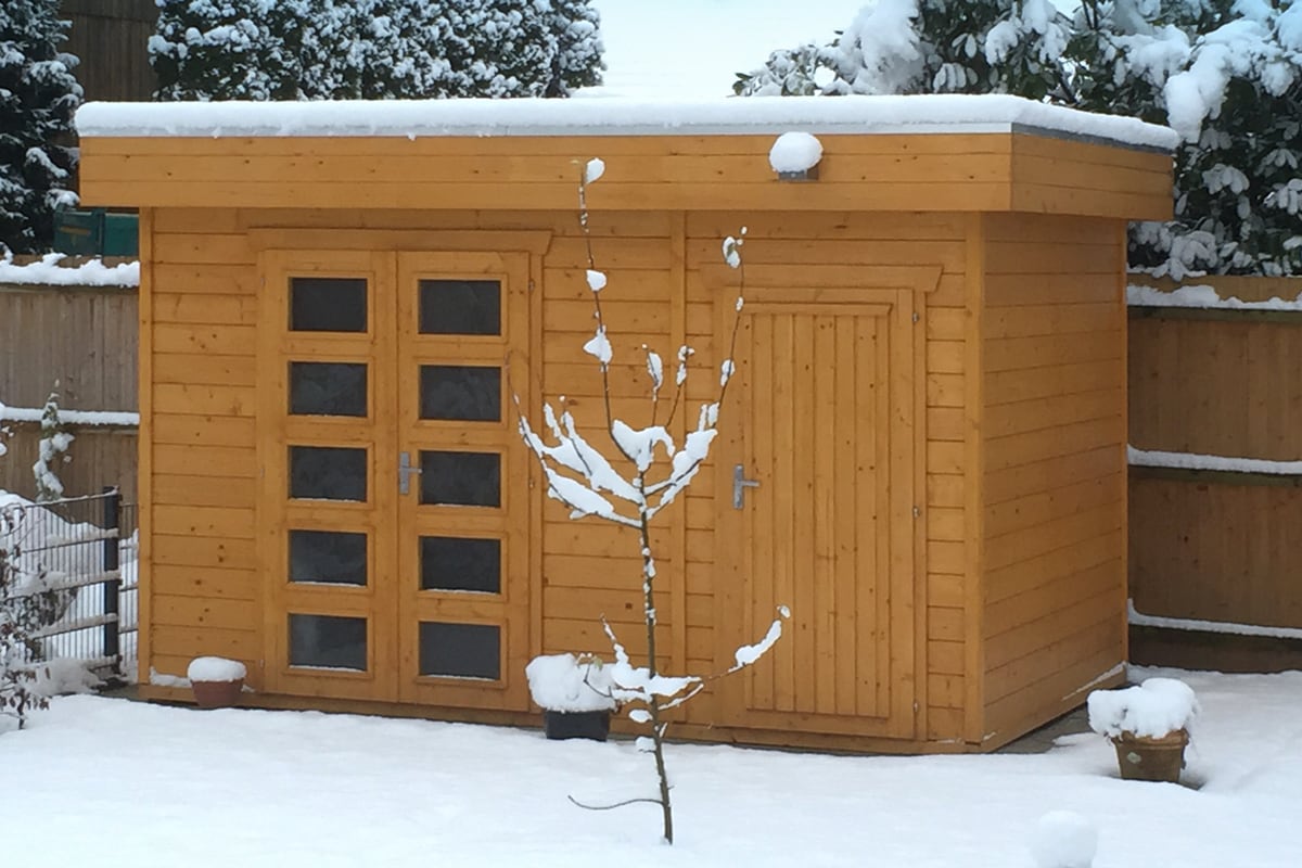 Holz-Gartenhaus Venlo 3 mit Flachdach und zwei Türen, umgeben von Schnee und einem kleinen Baum davor