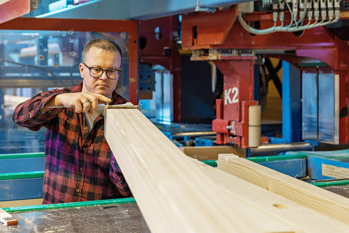 Person mit Schublehre die eine Holzbalken kontrolliert