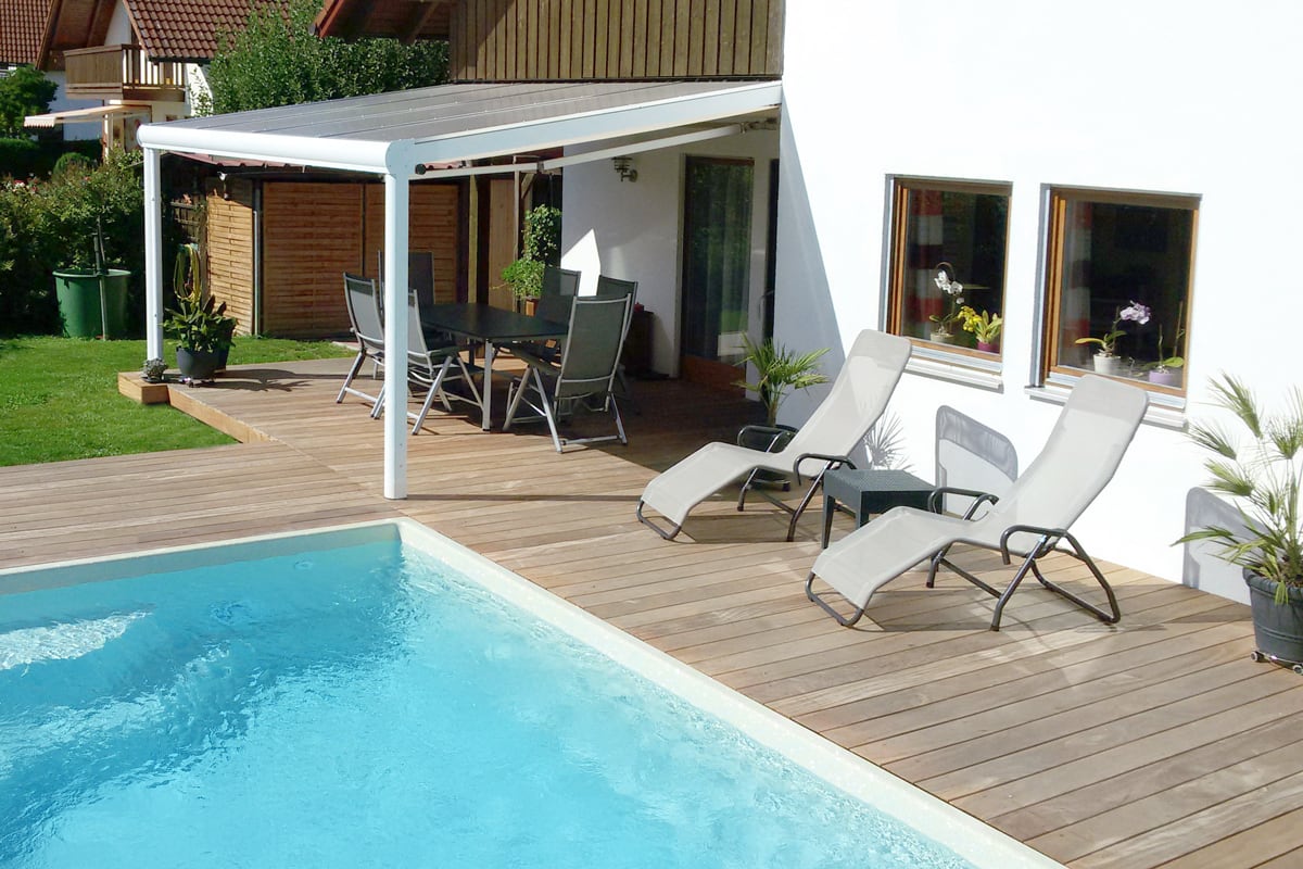 Eine moderne Terrassenüberdachung als Aluminium schafft eine einladende Verbindung zwischen Wohnraum, Garten und Poolbereich.
