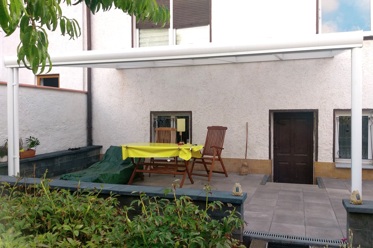 Weiße Terrassenüberdachung aus Aluminium mit einer Sitzgarnitur über einem Hauseingang.