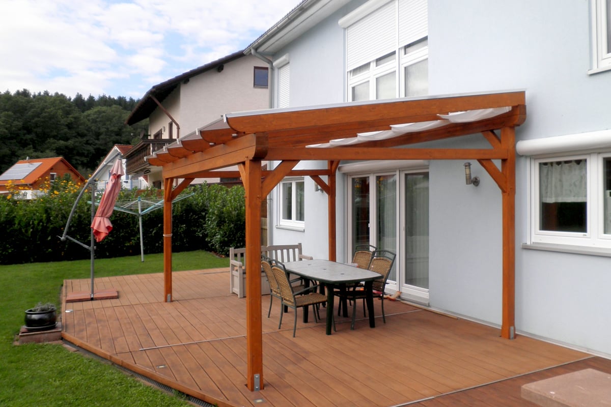 Eine moderne Holzterrasse mit Überdachung und Sitzgruppe bietet direkt am Haus einen geschützten Platz im Freien.
