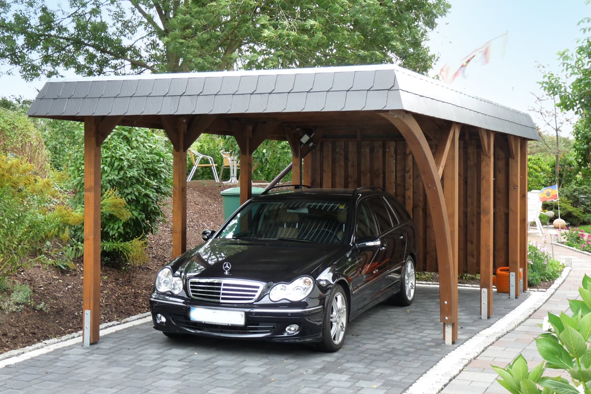 Walmdach-Carport mit schwarzer Blende und einem Einfahrtsbogen