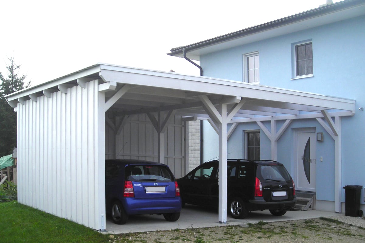 Geräumiges Carport aus robustem Holz mit seitlicher Verkleidung und Platz für zwei Fahrzeuge. Die weiße Lackierung und die stabile Konstruktion sorgen für ein harmonisches Gesamtbild und zuverlässigen Wetterschutz.