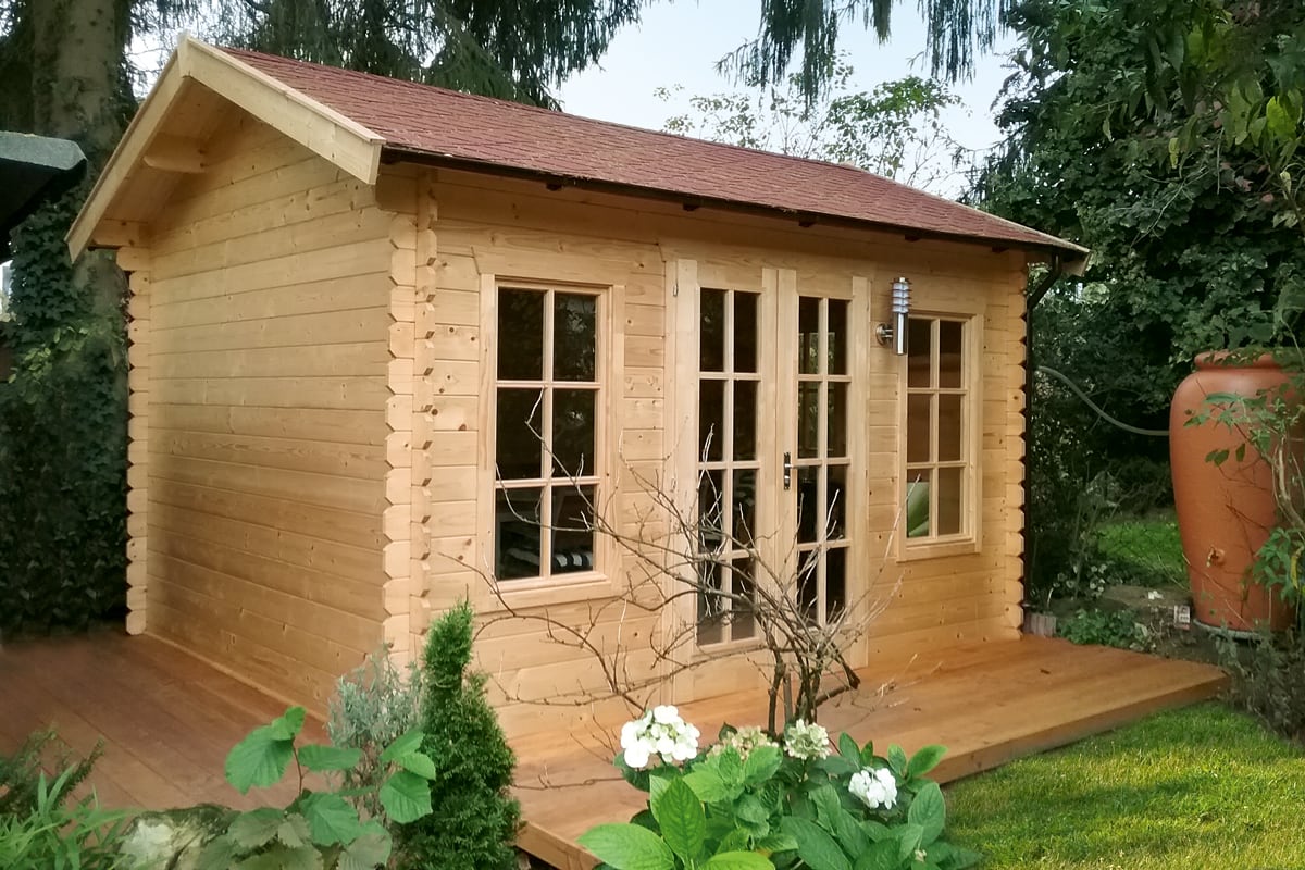 Holzhaus mit zwei Fenstern und einer Tür, umgeben von Gartenpflanzen und Bäumen