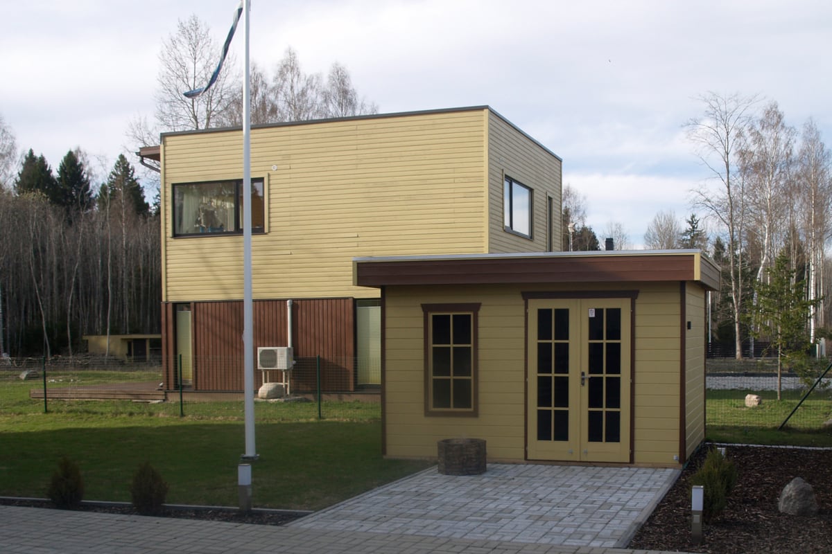 Gartenhaus Breda vor modernem zweistöckigen Haus mit gelber Holzverkleidung und kleinem Anbau mit Fenstern und Tür auf gepflastertem Weg