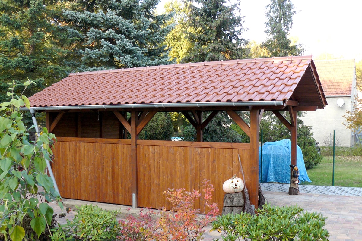 Hochwertiges Holzcarport mit traditionellem Satteldach und seitlicher Teilverkleidung für optimalen Wetterschutz. Die massive Konstruktion und das Ziegeldach sorgen für Langlebigkeit und eine harmonische Integration in die Umgebung.
