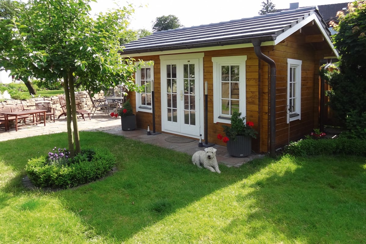 Holzhaus in einem Garten mit Rasen und Hund davor