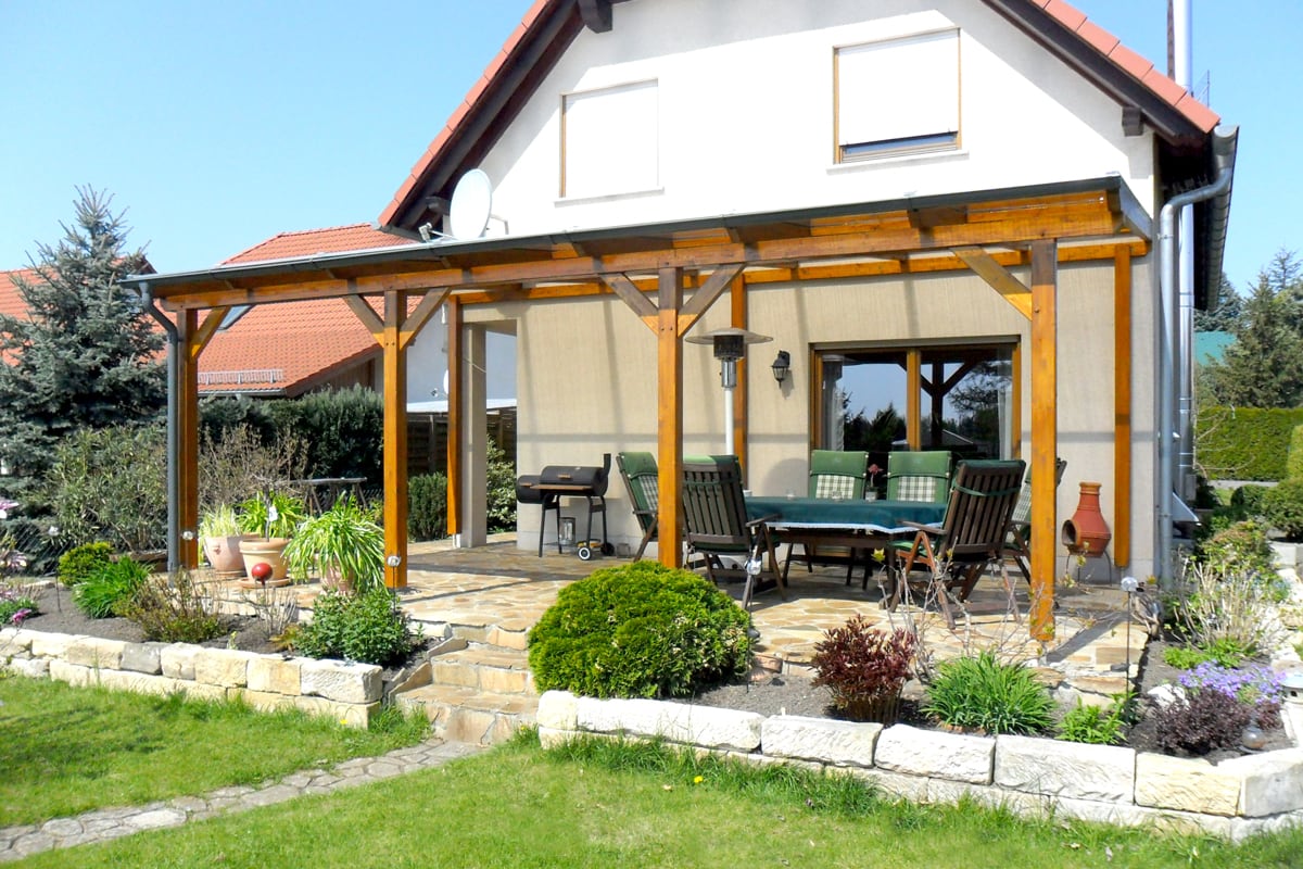Eine großzügige Terrassenüberdachung aus Holz schafft am Haus einen geschützten Ess- und Grillbereich mit Blick in den Garten.