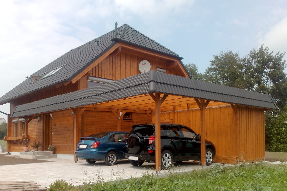 Großzügiges Carport aus hochwertigem Holz mit integriertem Abstellraum und passender Dachgestaltung zum Wohnhaus. Die massive Konstruktion bietet stabilen Schutz für Fahrzeuge und fügt sich harmonisch in die Hausarchitektur ein.