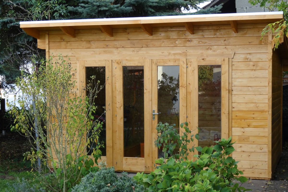Holz-Gartenhaus Ostende mit drei Glastüren, umgeben von grünen Pflanzen und Büschen