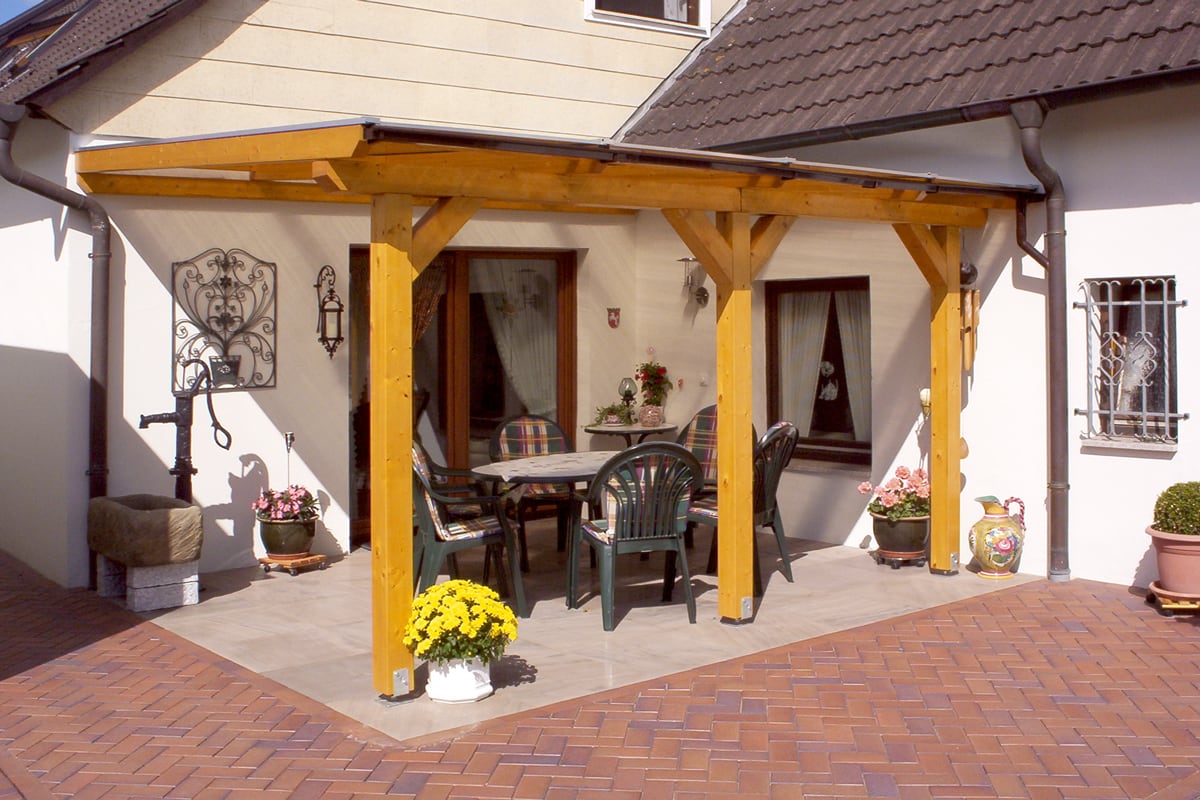 Eine Terrassenüberdachung aus Holz mit Sitzgruppe direkt am Haus.