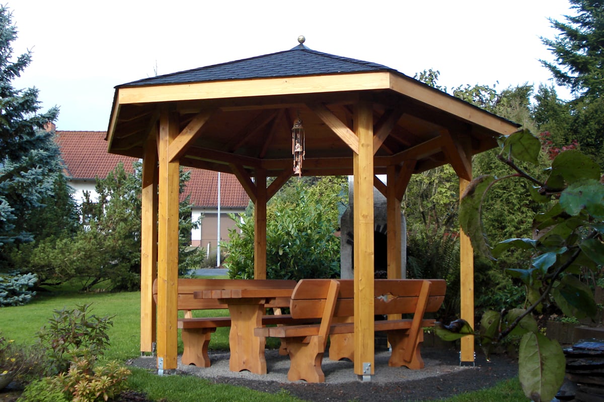Sechseckiger Holzpavillon mit massiven Gartenmöbel aus Holz darunter.