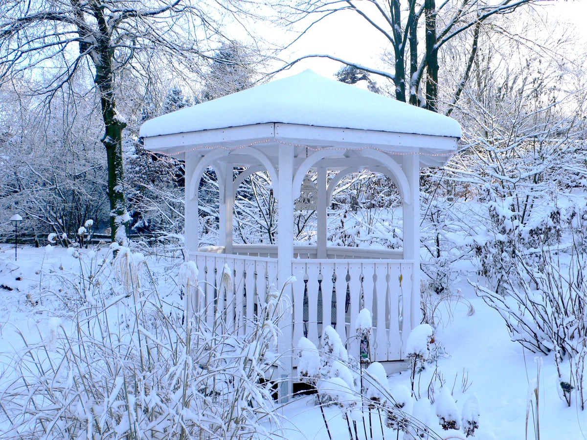 Sechseckiger weißer Holzpavillon im Winter mit Schnee auf dem Dach.