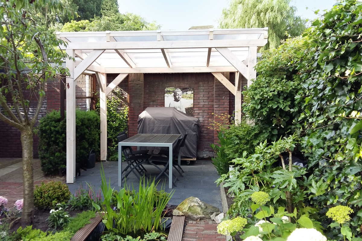 Ein heller Holzpavillon mit transparentem Dach fügt sich harmonisch in den grünen Garten ein. Darunter bietet ein Esstisch mit Stühlen einen geschützten Platz zum Entspannen oder Grillen.